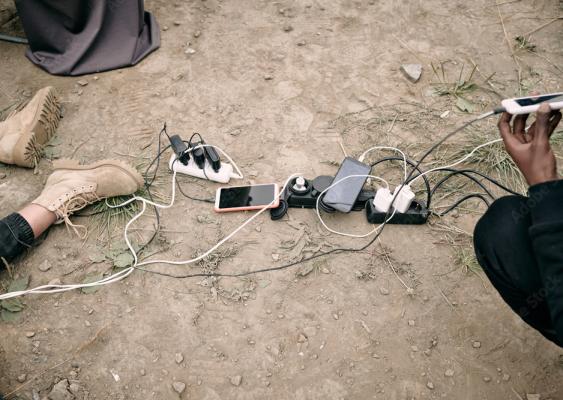 Cell phones with charger cables plugged into power bars on the ground outdoors