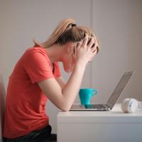 Teen girl sitting at a computer holding her head in her hands