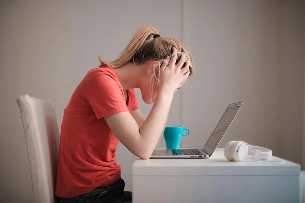 Teen girl sitting at a computer holding her head in her hands